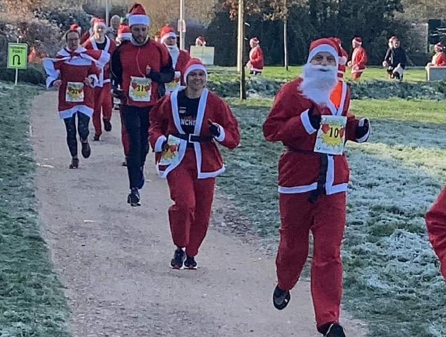 A group of runners dressed in Santa suits with white beards and red hats participating in a festive race.